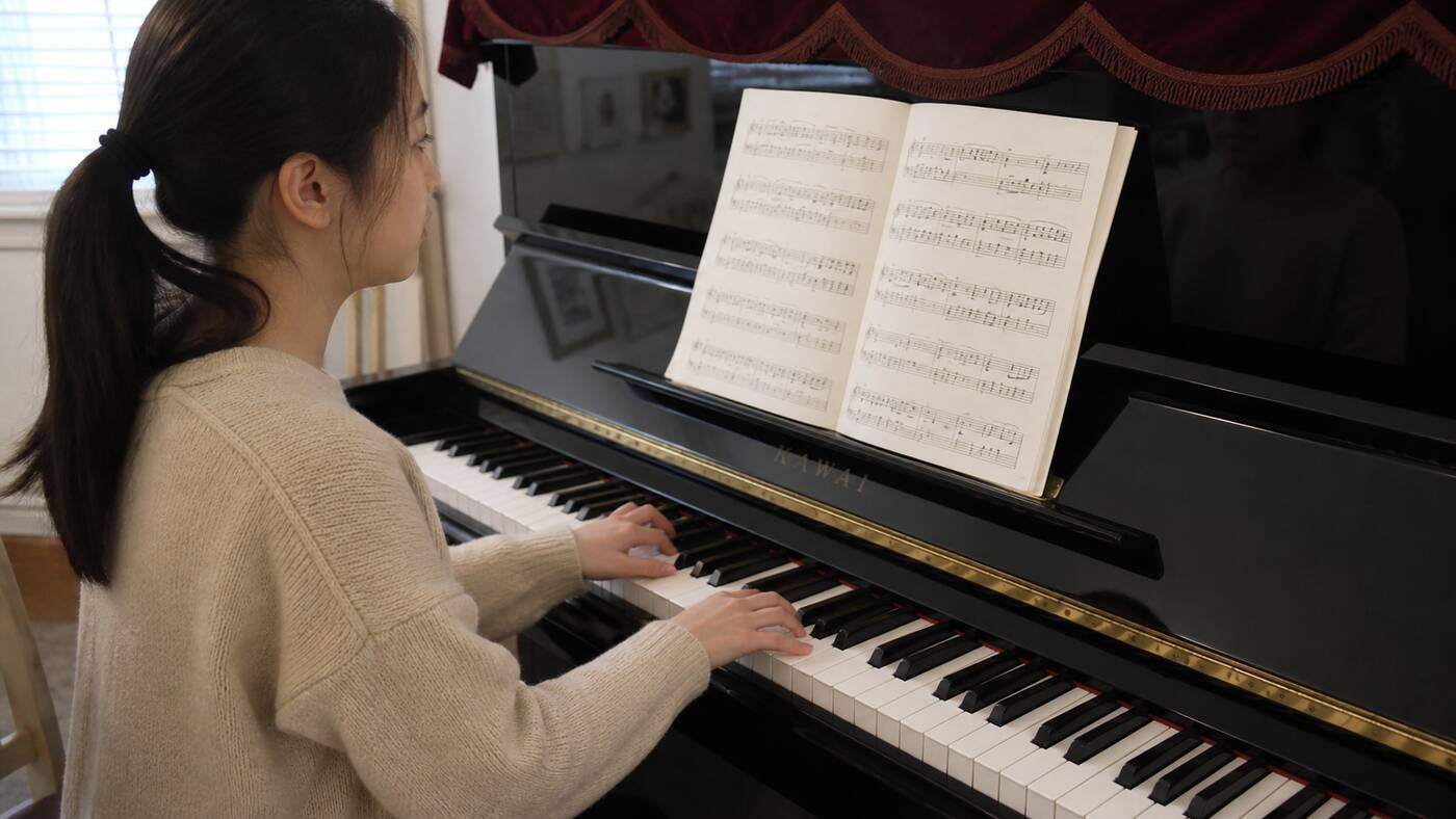 Pianist sight-reading sheet music on an upright Kawai piano